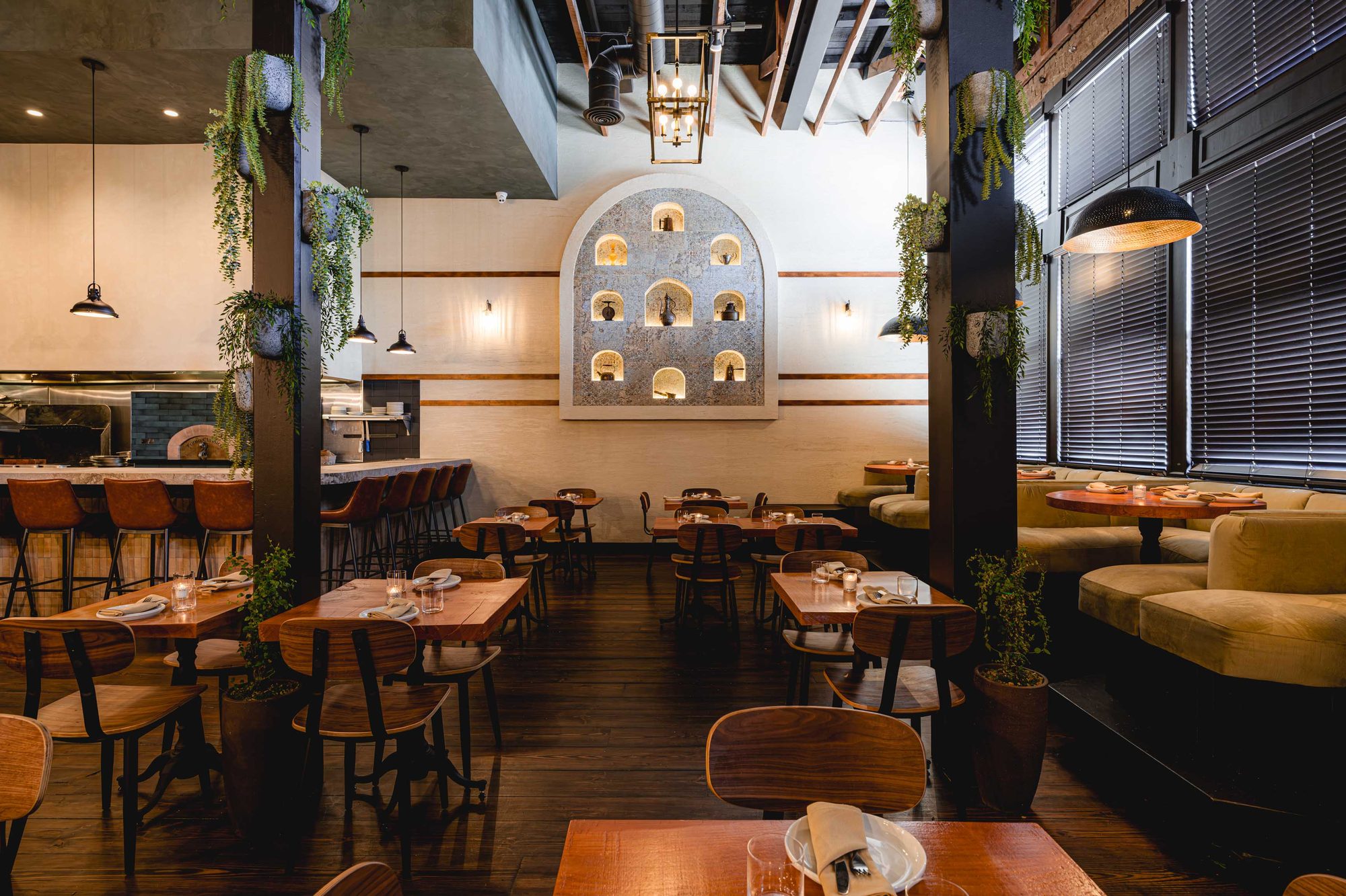 Carmel restaurant dining room in Los Angeles with brick, timber tables, hanging greenery and an arched display niche