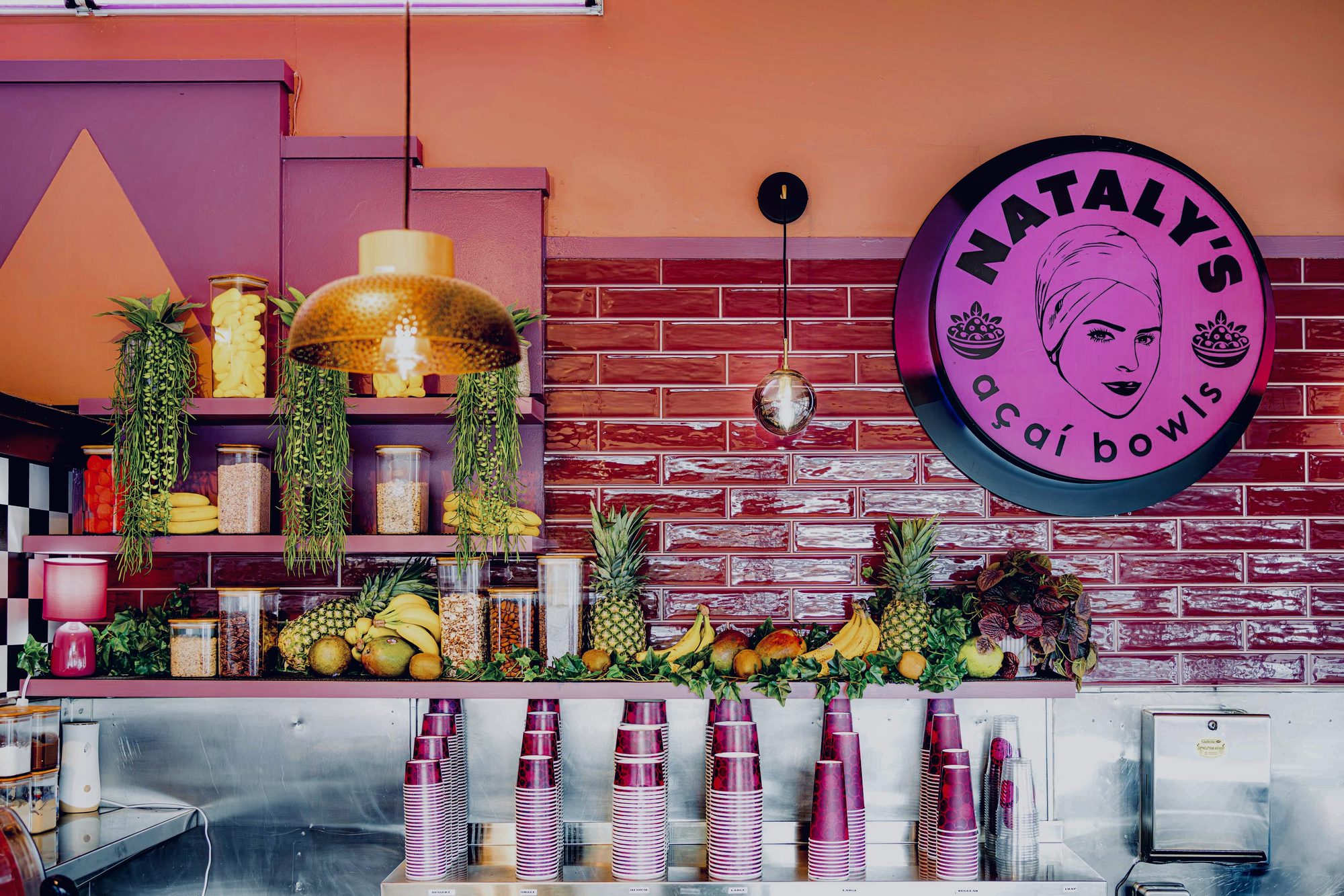 Nataly's Acai bar with magenta brick wall, neon logo and fruit display